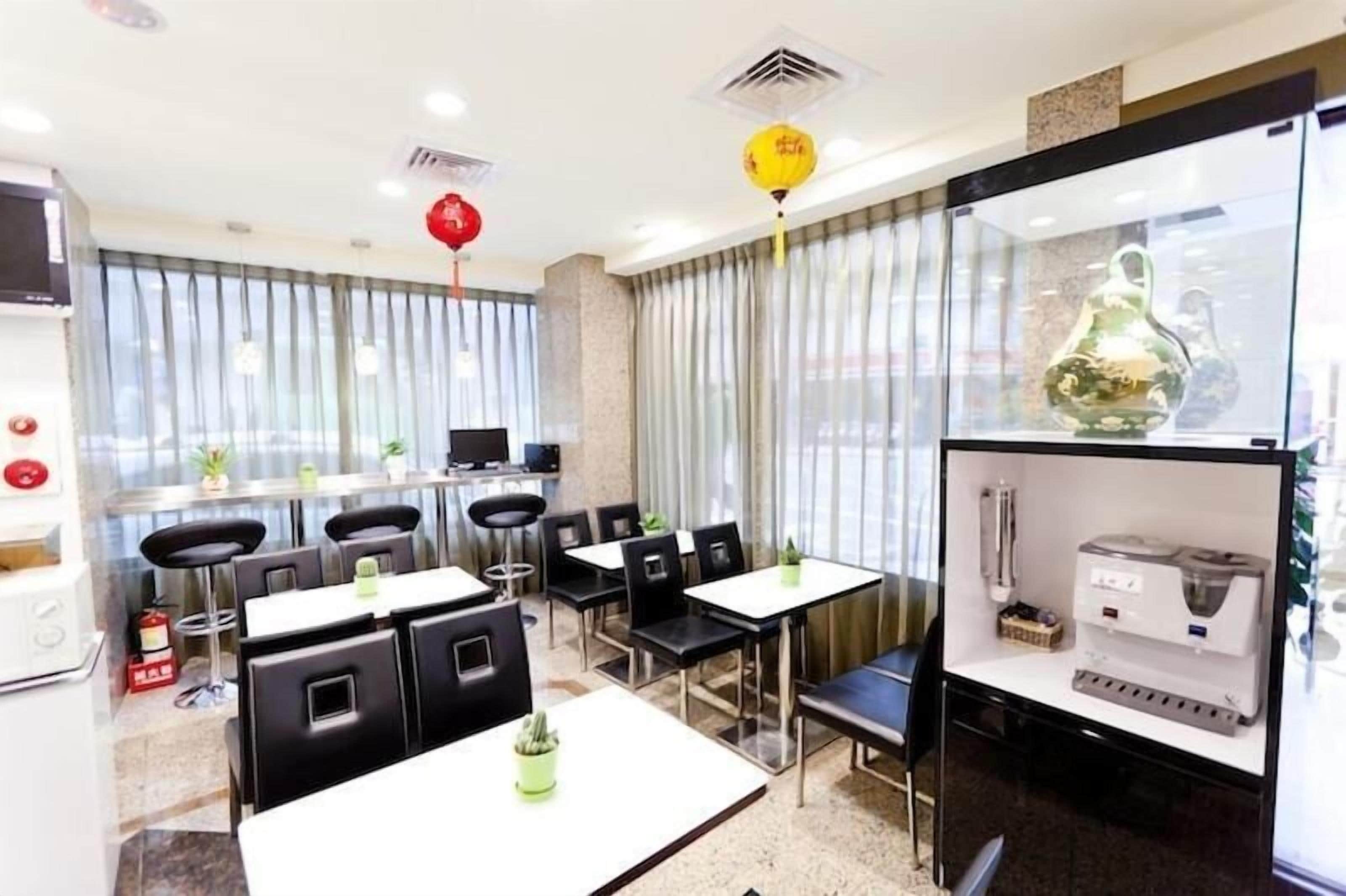 Un comedor de hotel con mesas y sillas, una zona de cocina con electrodomésticos y un amplio ventanal con cortinas.