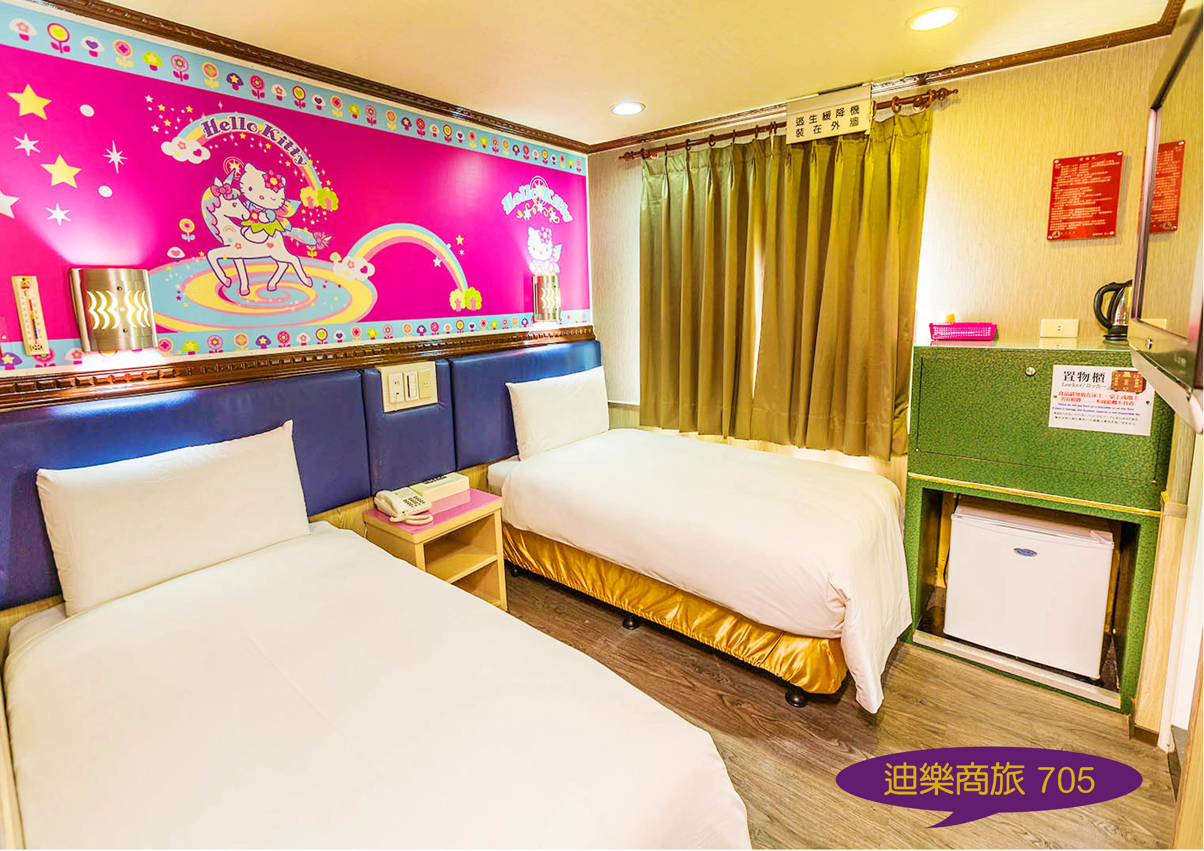 Una habitación de hotel con dos camas, una pared rosa decorada con motivos de Hello Kitty, una pared verde con un letrero y un refrigerador pequeño.