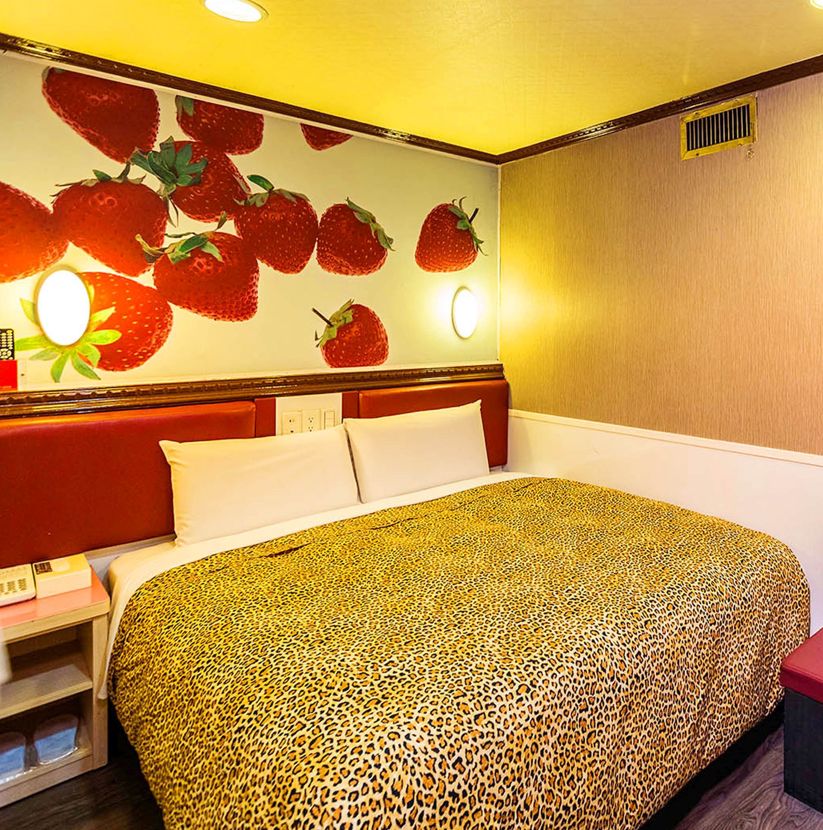 A hotel room with a bed, a nightstand, and a wall decorated with strawberries.