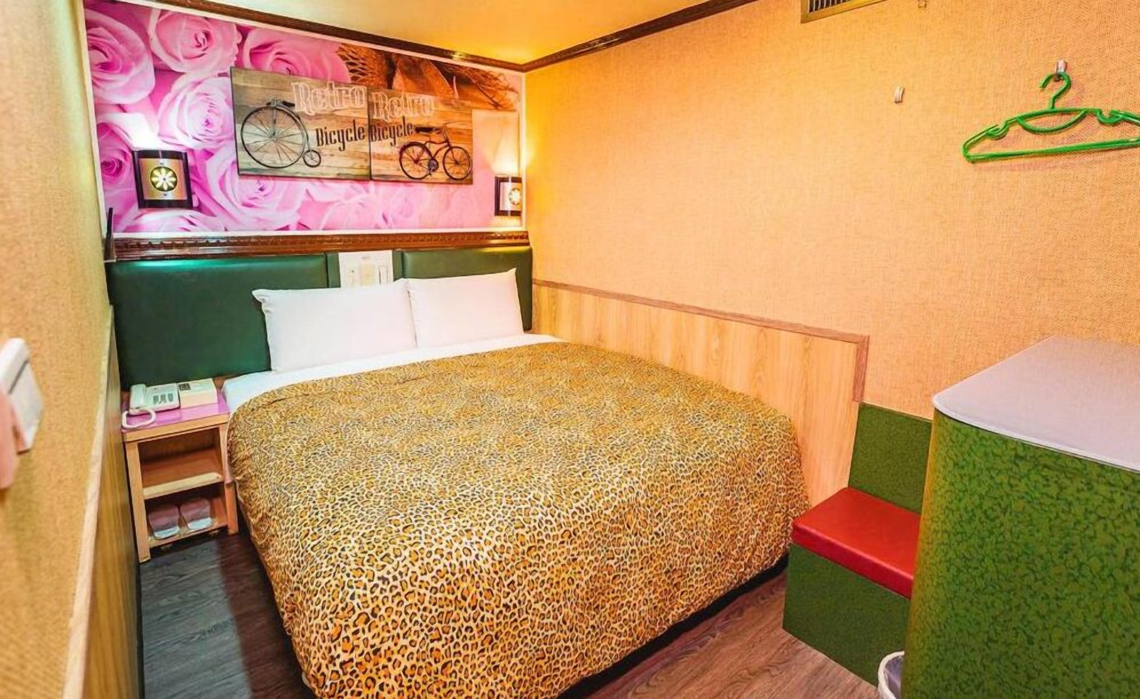 A bedroom with a leopard print bedspread, a headboard with a clock, a wall-mounted bicycle decoration, and a green and red bathroom area.