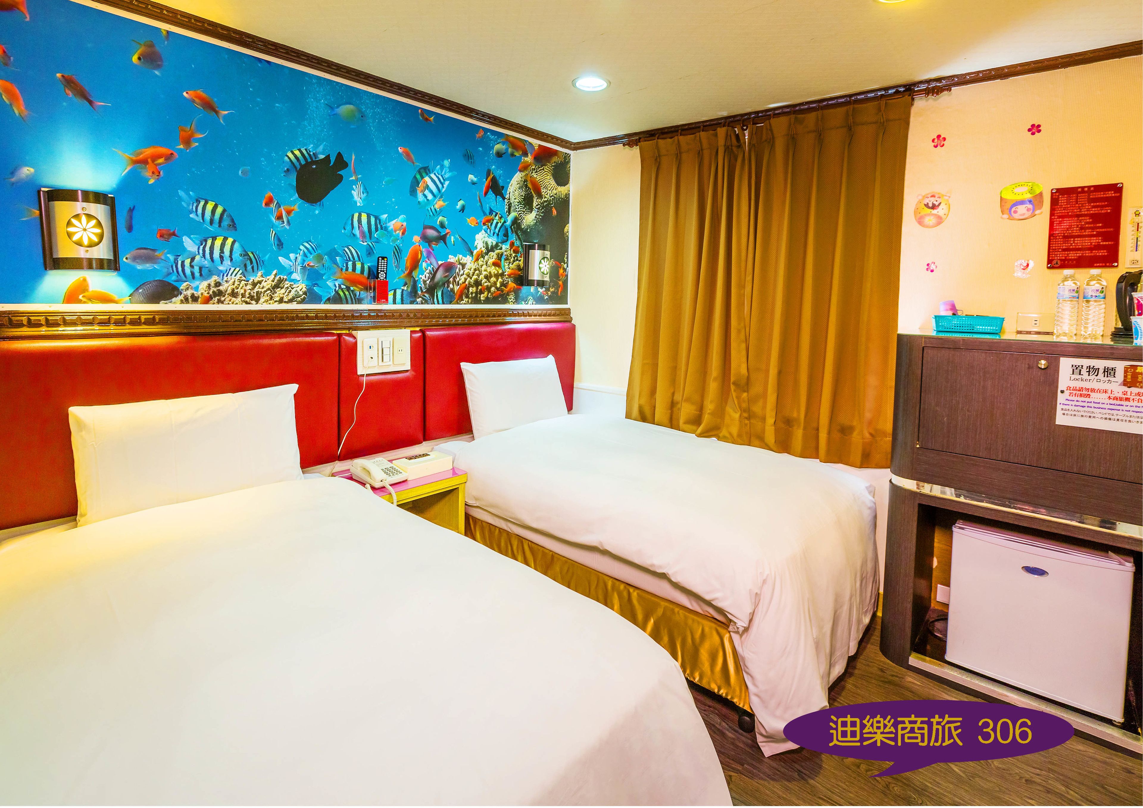 Une chambre d’h ôtel avec deux lits, une tête de lit rouge, une fresque murale représentant des poissons, une armoire en bois et un panneau avec du texte en japonais.