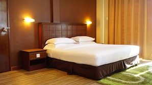 A hotel room with a wooden headboard, a wooden nightstand, a green area rug, and two wall-mounted lights.