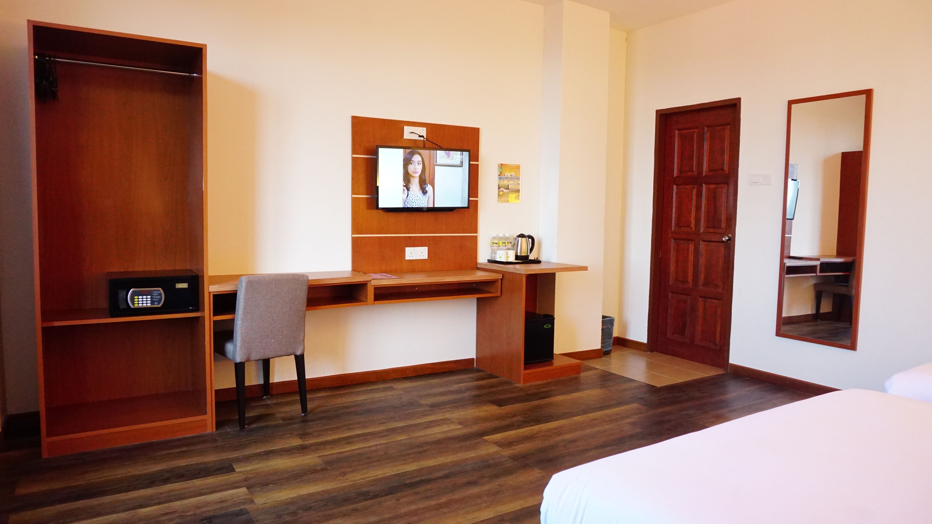 Una habitación de hotel con un escritorio de madera, una silla, una cama, un armario, un televisor y un espejo.