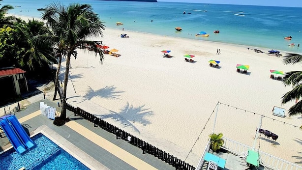 A beach with a pool, umbrellas, and palm trees.