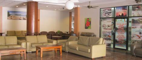 A lobby with leather sofas, a wooden coffee table, and a glass display of travel posters.