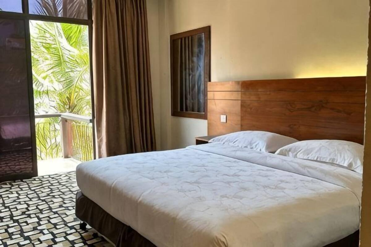 A double bed with a wooden headboard, a nightstand, and a window with curtains.