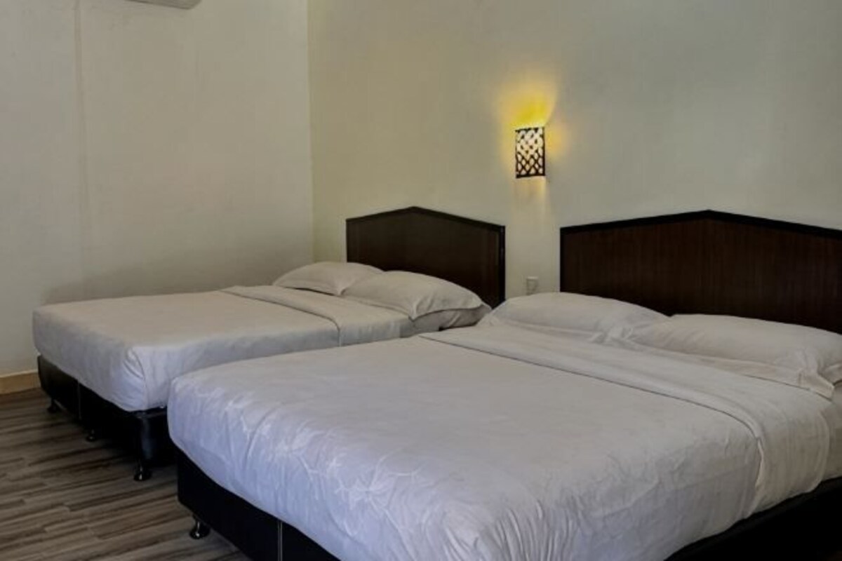 Habitación de hotel con dos camas, cabecera y lámpara fijada a la pared.
