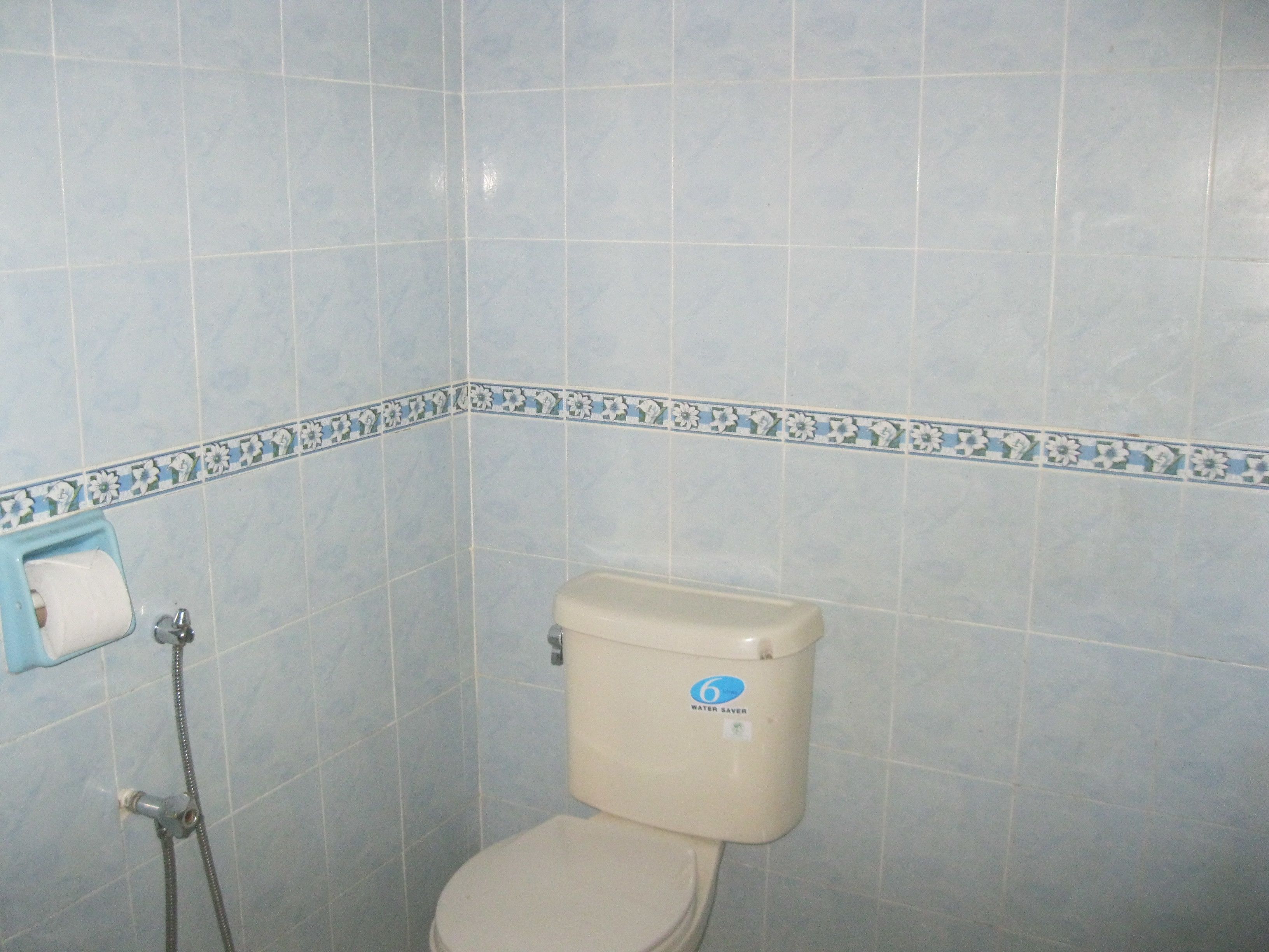 Un baño con azulejos azul claro, un inodoro con etiqueta de ahorro de agua y un dispensador de toallas de papel.