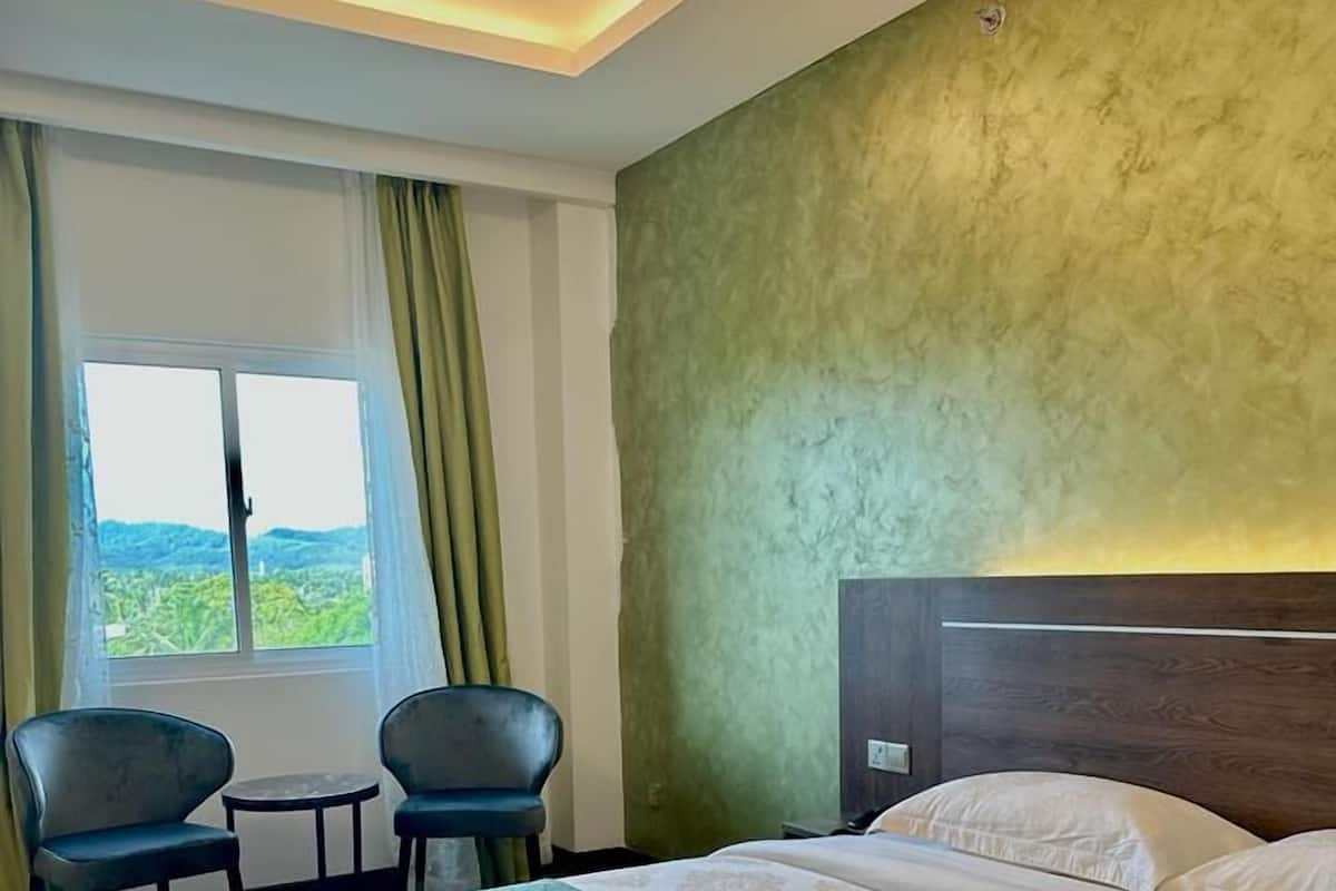 A hotel room with a large bed, two chairs, a small table, and a window with a view of greenery.