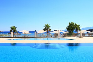 A clear blue pool with umbrellas and palm trees, surrounded by a beach view. - Palm Bay Beach Hotel (Datça)