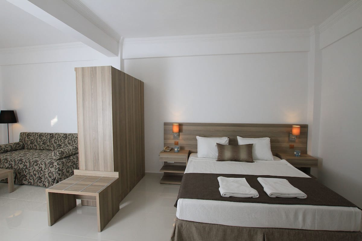 Una habitación de hotel moderna con una cama, mesitas de noche, un sofá y un pequeño banco de madera.