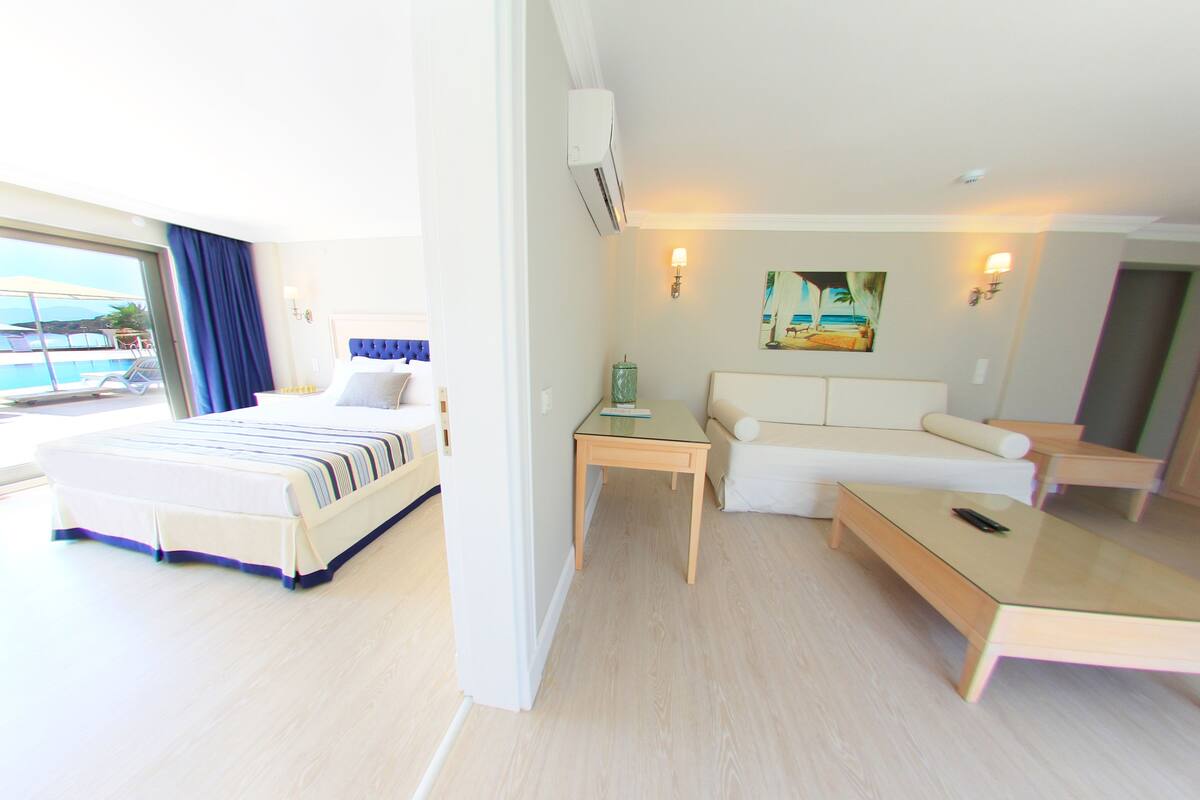 Habitación de hotel con cama, sofá, una mesita y vista al mar.