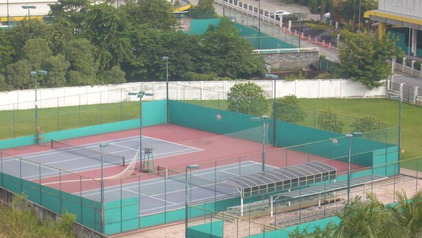 A tennis court with a green fence, a covered seating area, and trees in the background. - DMK Donmueang Airport Guesthouse (Pak Kret)