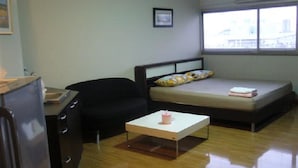 A compact room with a bed, a small desk, a chair, and a window. - DMK Donmueang Airport Guesthouse (Pak Kret)