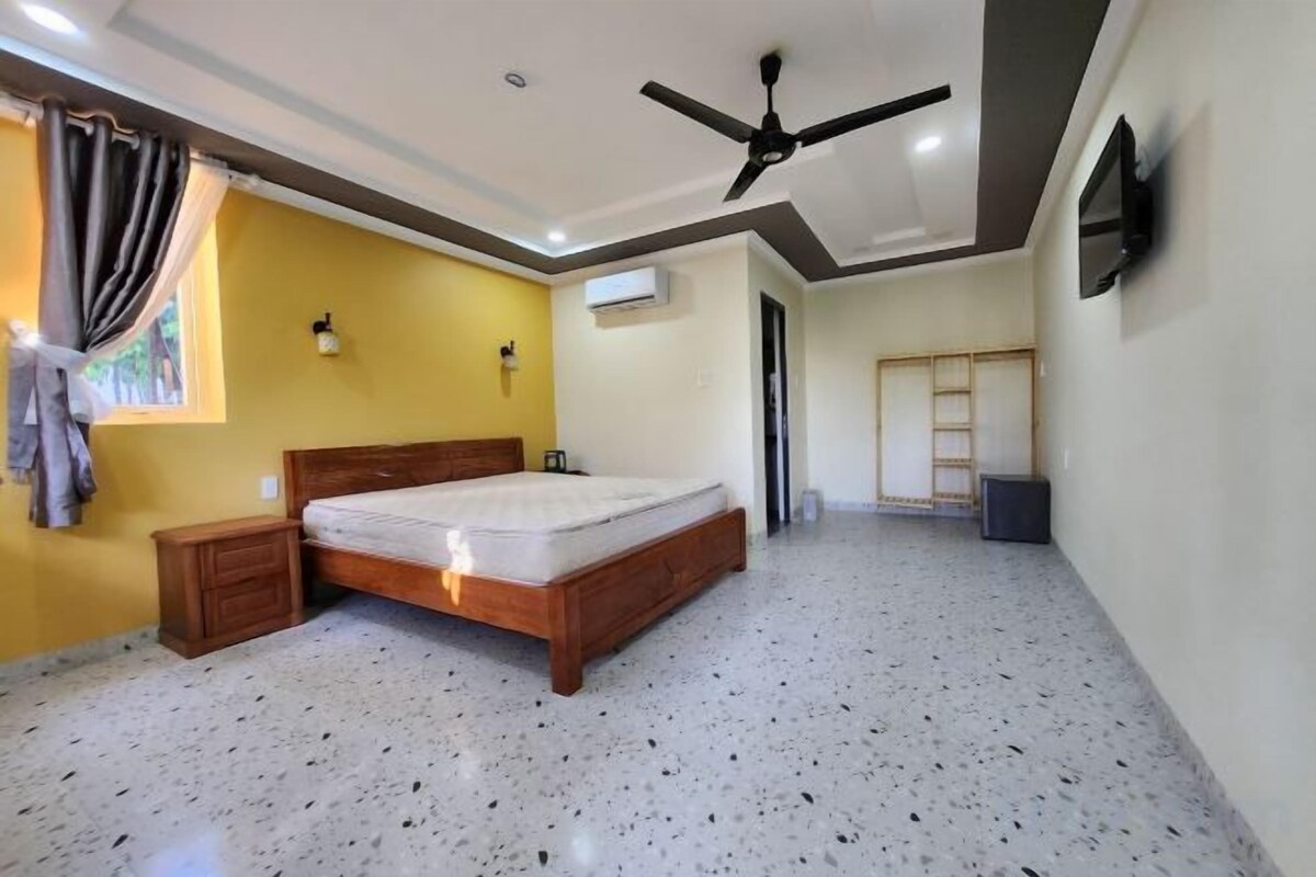 Un dormitorio con cama, ventilador de techo, ventana con cortinas y puerta que da a otra habitación.