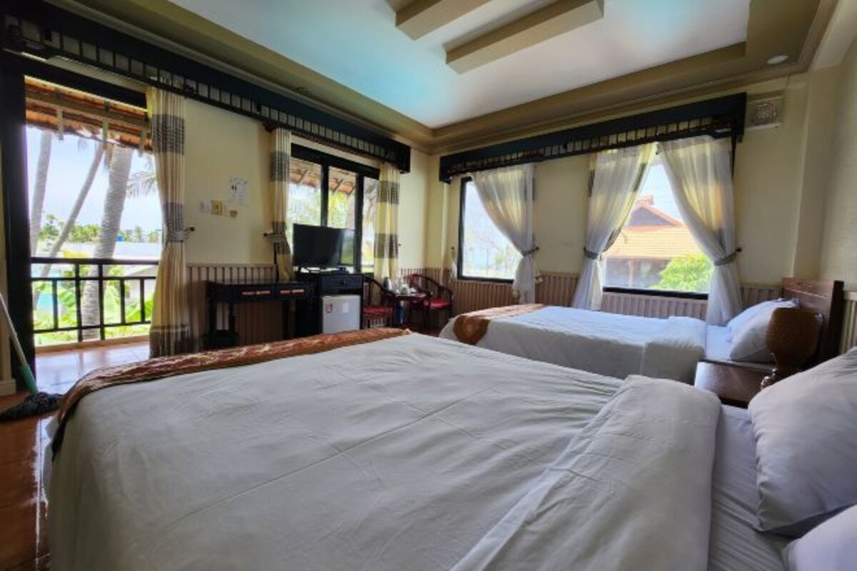 A hotel room with two beds, a TV, and a balcony with curtains.
