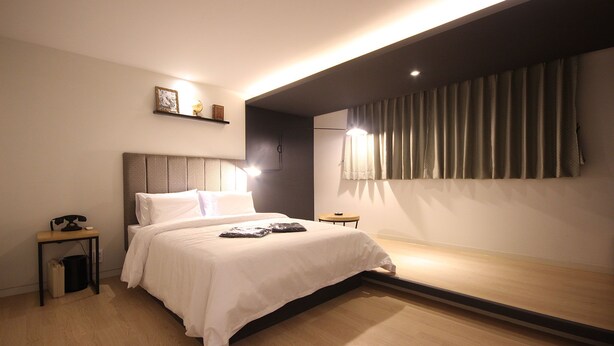 A modern hotel room with a large bed, bedside table, and a small table with a lamp.