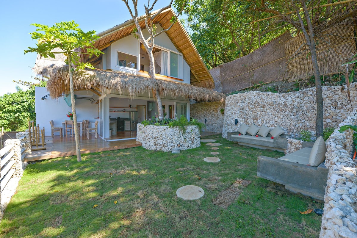 Una casa con techo de paja, paredes de piedra y un camino de piedra que conduce a una zona de estar.