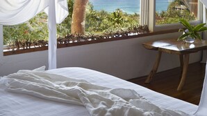 A bedroom with a bed, a wooden table, and a view of the ocean through sheer curtains.