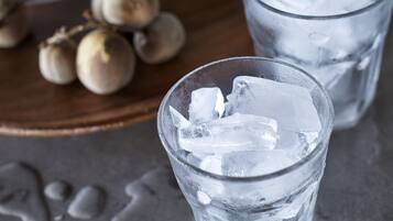 Two glasses of water with ice cubes on a wooden surface, a bottle of water, and some hazelnuts in the background.