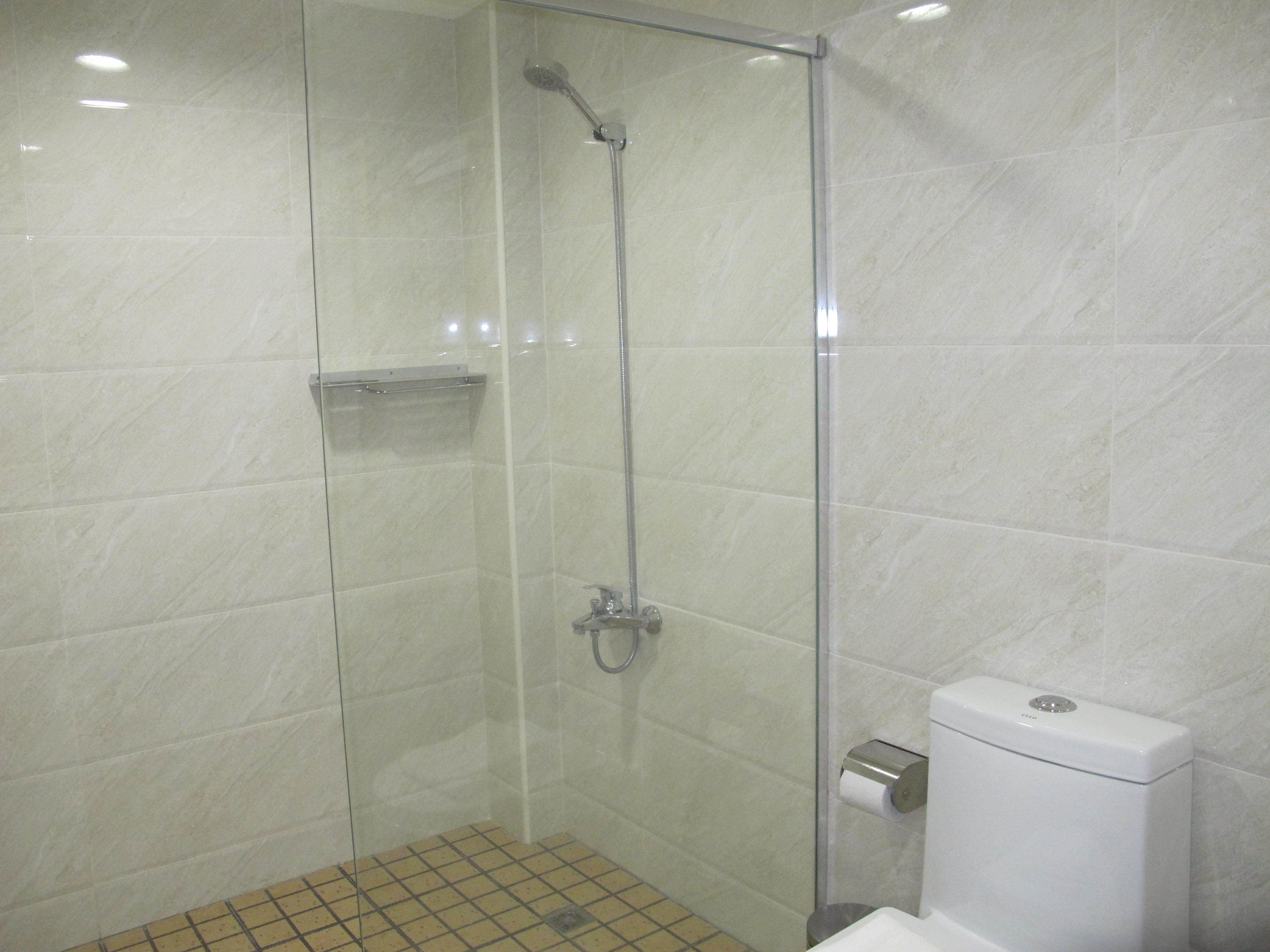 Cabina de ducha con vidrio, inodoro y dispensador de toallas de papel.