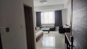 A modern hotel room with a large bed, a sofa, a desk, and a view of the city through large windows. - Townhouse Oak Vera Hotel Near Clark International Airport (Angeles City)