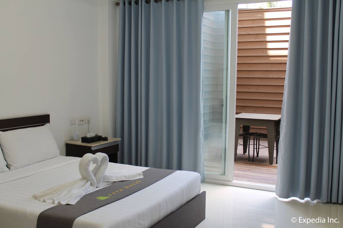 Habitación de hotel con cama, mesita de noche, escritorio y vista a un patio exterior.