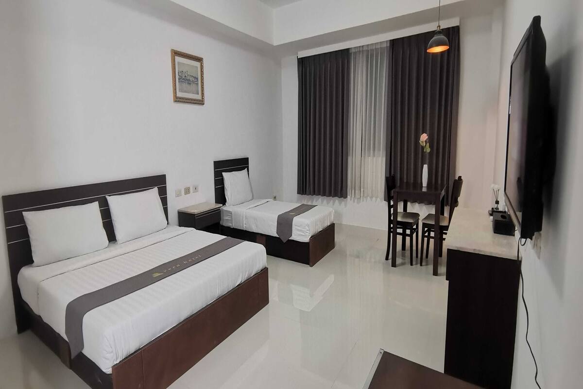 Habitación de hotel con dos camas, un escritorio, una silla, un televisor y una ventana con cortinas.