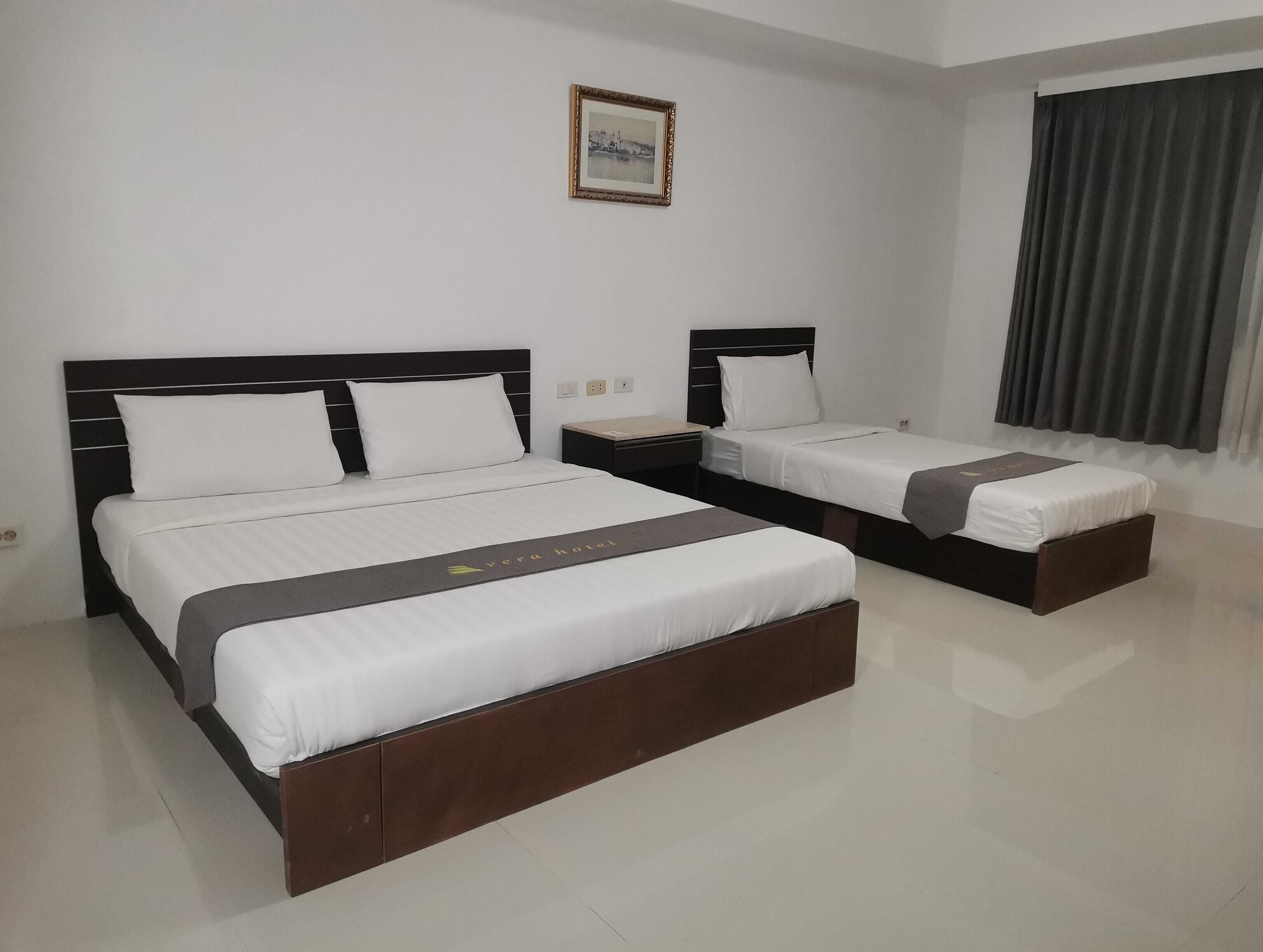 A hotel room with two beds, a nightstand, a framed picture on the wall, and a window with curtains.