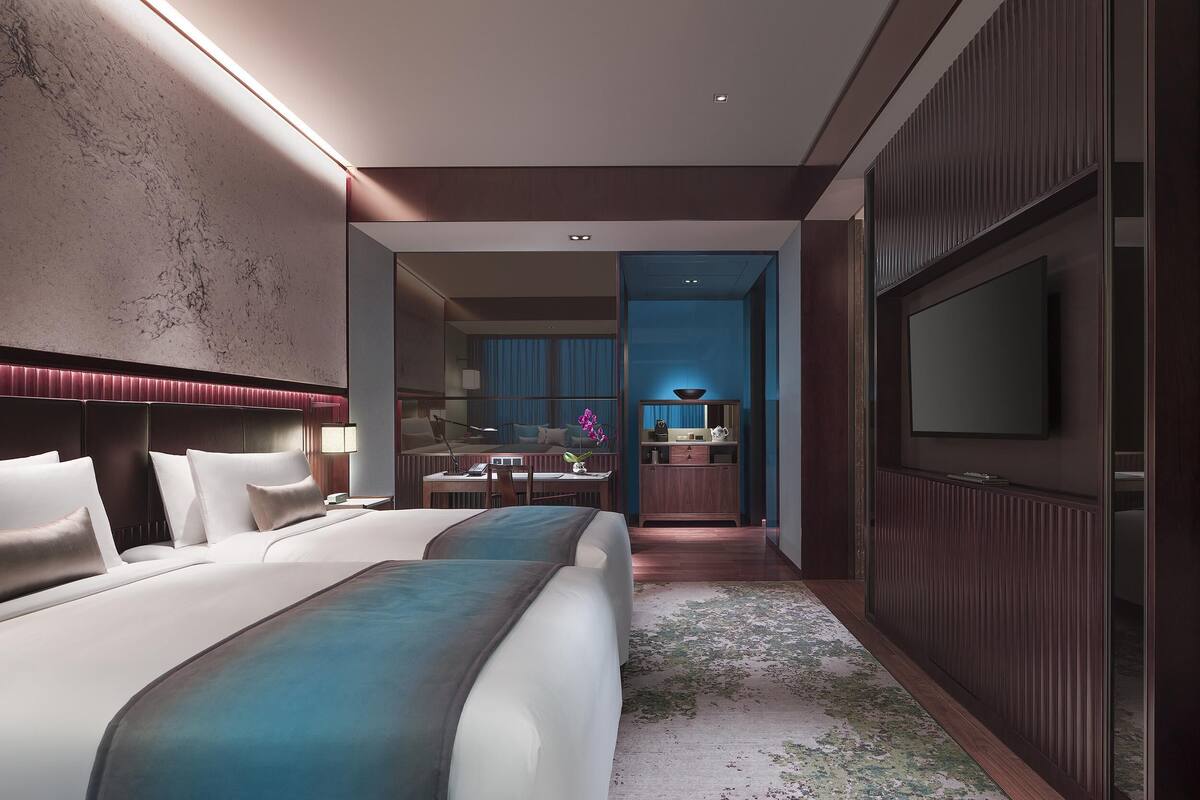 A modern hotel room with a large bed, a desk, a TV, and a bathroom visible through an open door.