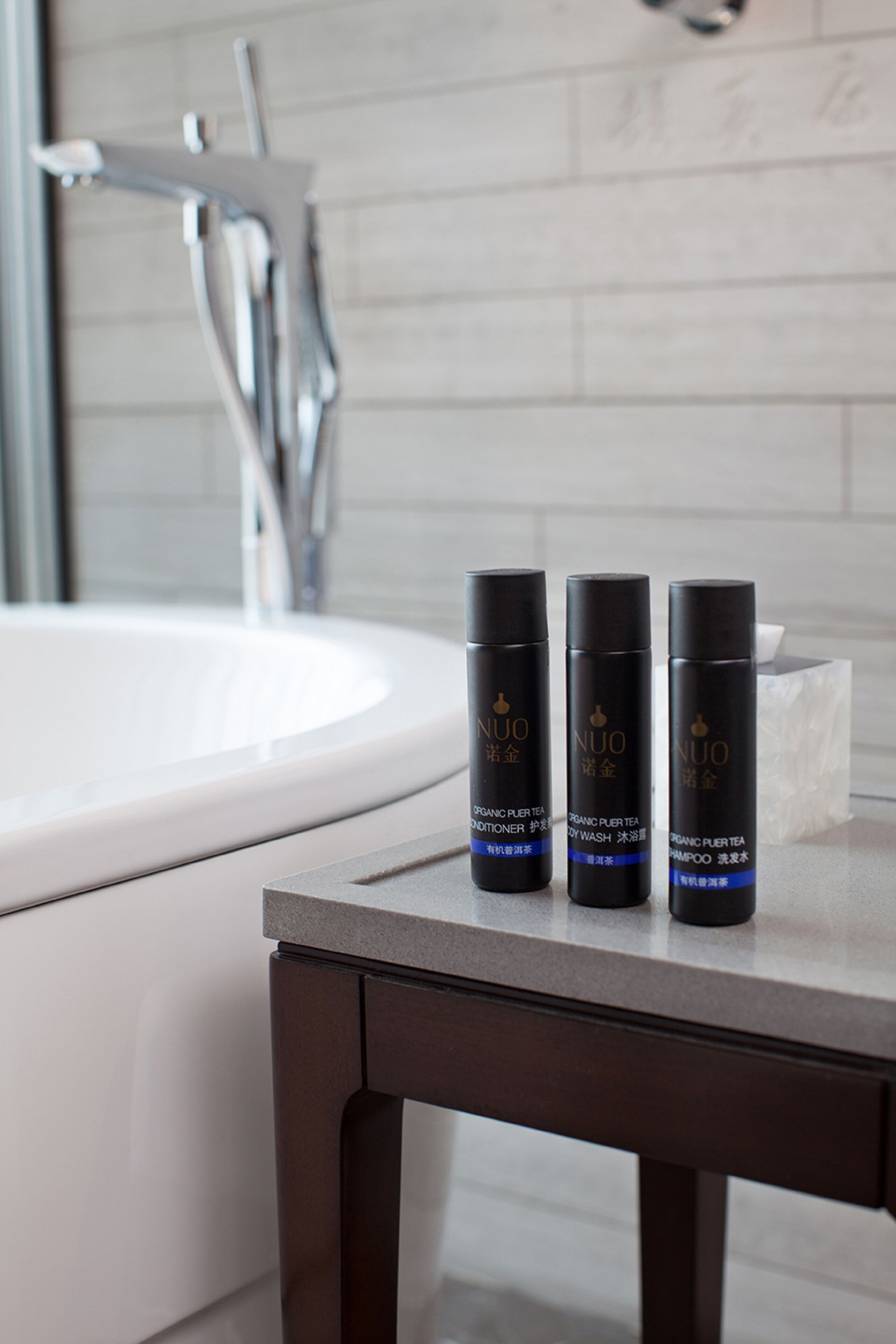 A bathroom with a white sink, a mirror, and three black bottles of NUO organic hair wash and shampoo on a dark wooden table.