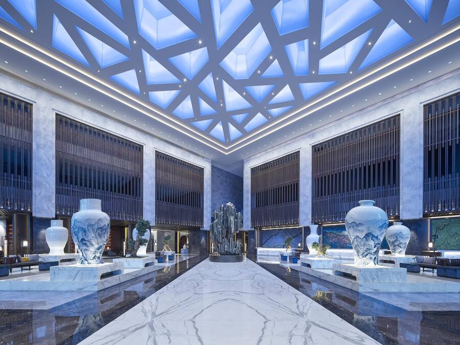 A spacious lobby with a high ceiling, large windows, and a central marble floor.