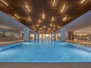 Une grande piscine intérieure dotée d’un plafond au design moderne et d’un espace dédié aux exercices sur l’un des côtés.