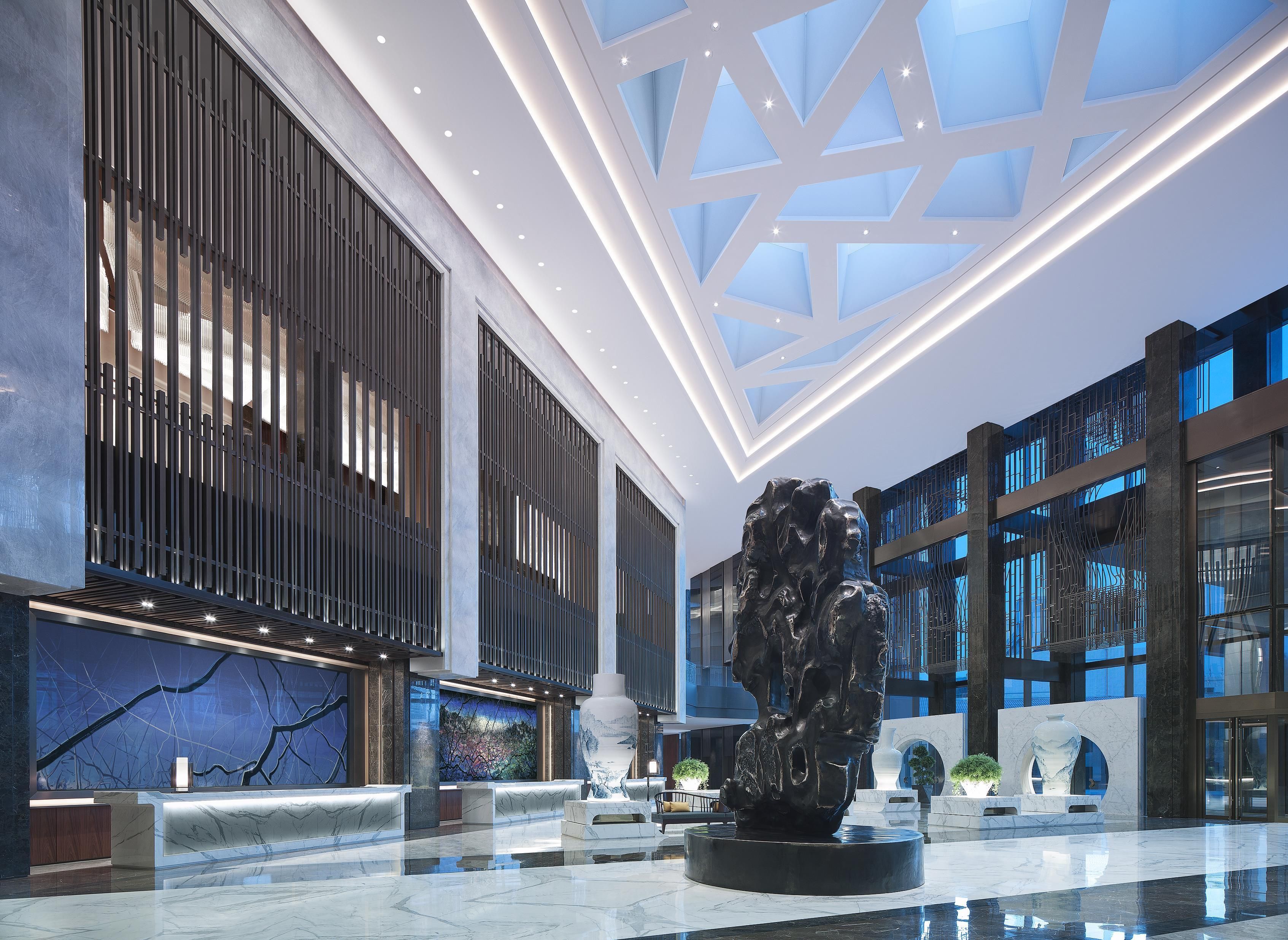 A spacious lobby with a high ceiling, modern lighting, and a central sculpture.