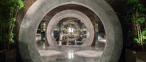 Una estructura arquitectónica circular con un espacio central abierto, rodeada de follaje y superficies reflectantes.