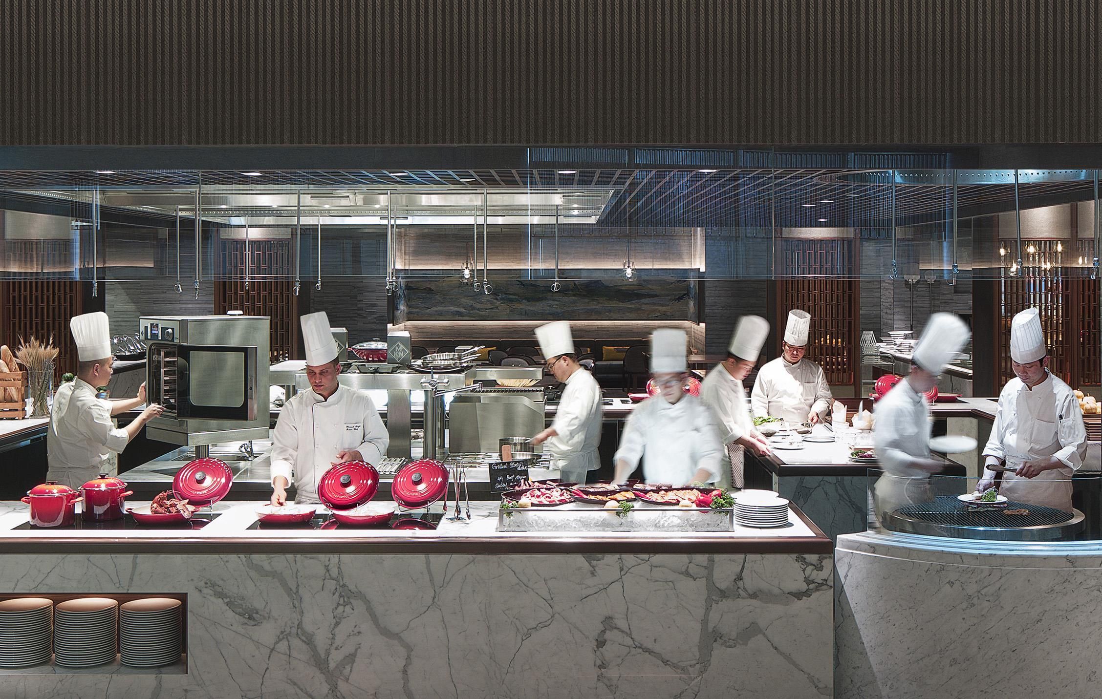 A modern kitchen with chefs preparing food, stainless steel appliances, and marble countertops.