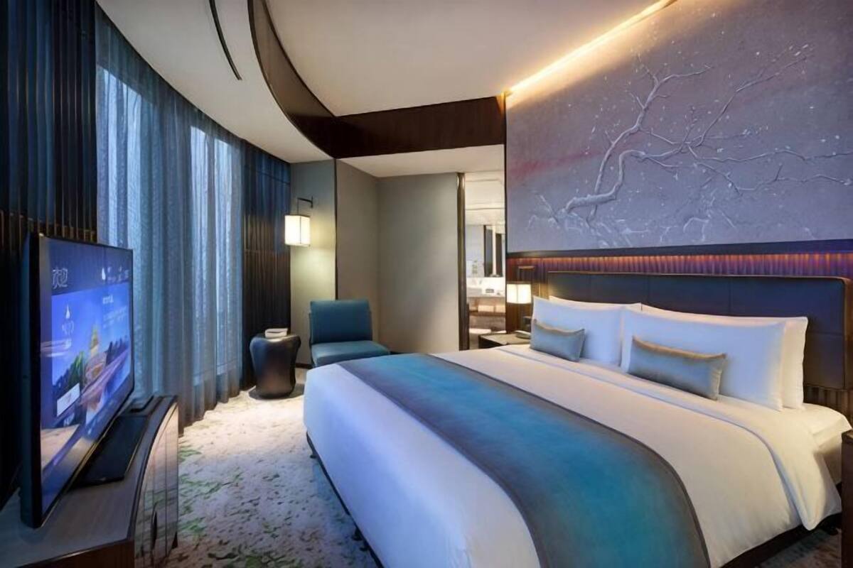A modern hotel room with a large bed, a television, a seating area, and a decorative wall.
