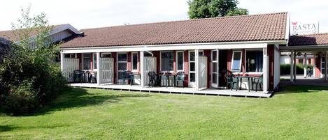 Un edificio de dos pisos con tejado de tejas rojas, un área de estar al aire libre techada con mesas y sillas, y un letrero que dice 'Rasta Country Kitchen'.
