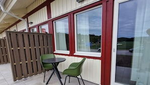 An outdoor seating area with a table and two chairs, a wooden fence, and a building with large windows and a red frame. - Nordby Hotell (Stromstad)