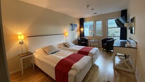 A hotel room with two beds, a desk, a chair, and a small table. - Nordby Hotell (Stromstad)