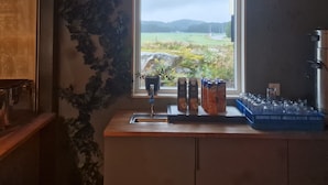 A kitchen with a window overlooking a rural landscape, a sink, and various containers on the counter. - Nordby Hotell (Stromstad)