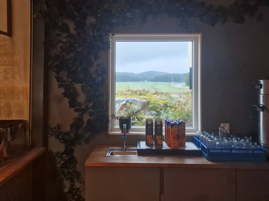 A kitchen with a window overlooking a rural landscape, a sink, and various containers on the counter.