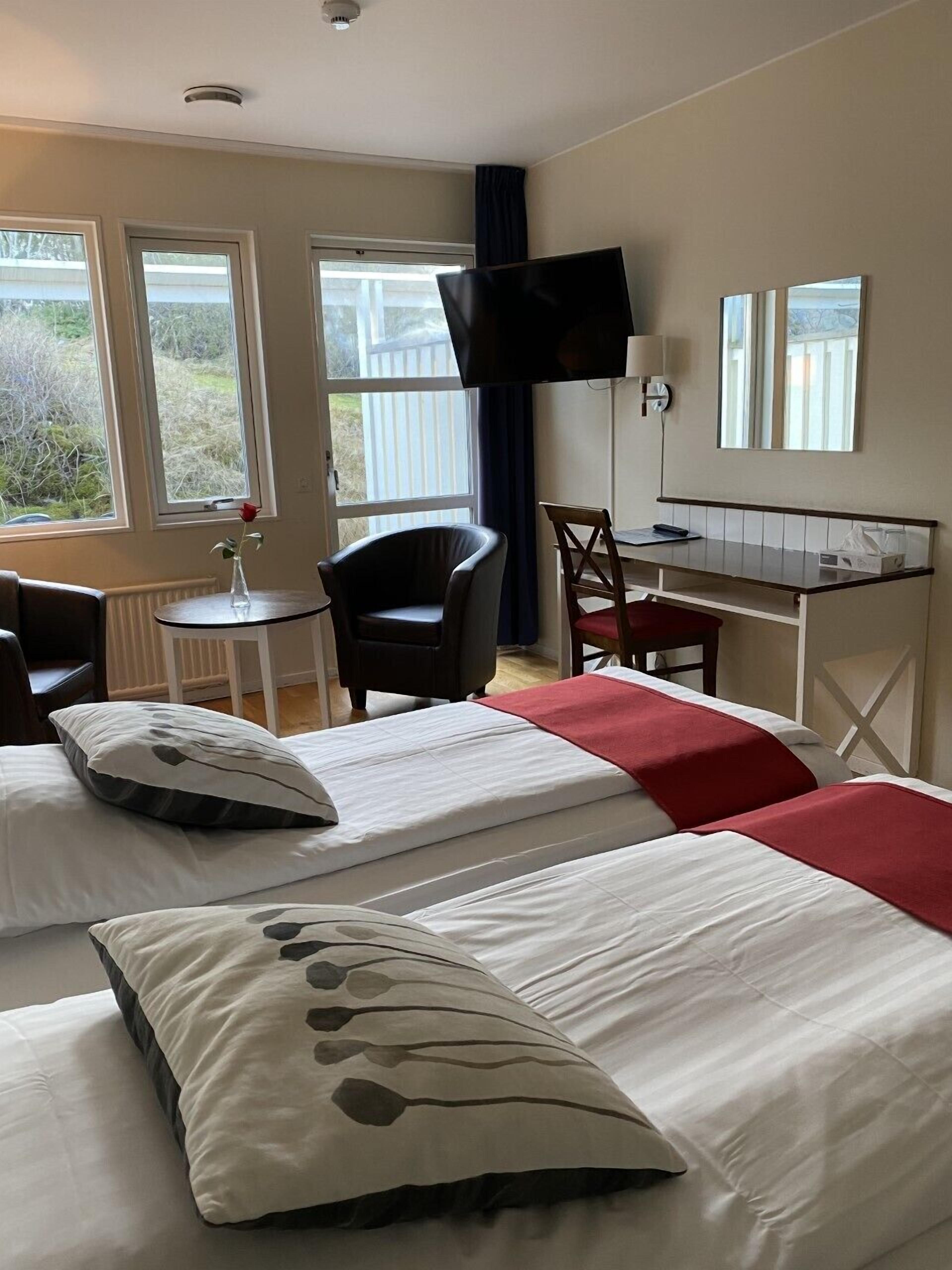 Ein Hotelzimmer mit zwei Betten, einem Schreibtisch, einem Stuhl, einem Fernseher und großen Fenstern.