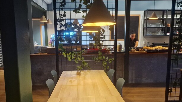 A modern dining area with a long wooden table, several chairs, hanging plants, and pendant lighting. - Nordby Hotell (Stromstad)