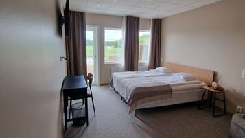 Une chambre d’hôtel avec un lit, un bureau, une chaise, une petite table et une fenêtre avec des rideaux.