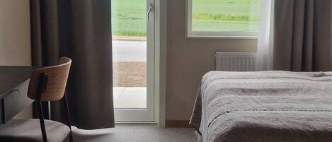 A hotel room with a bed, a chair, a window with curtains, and a view of a green field.