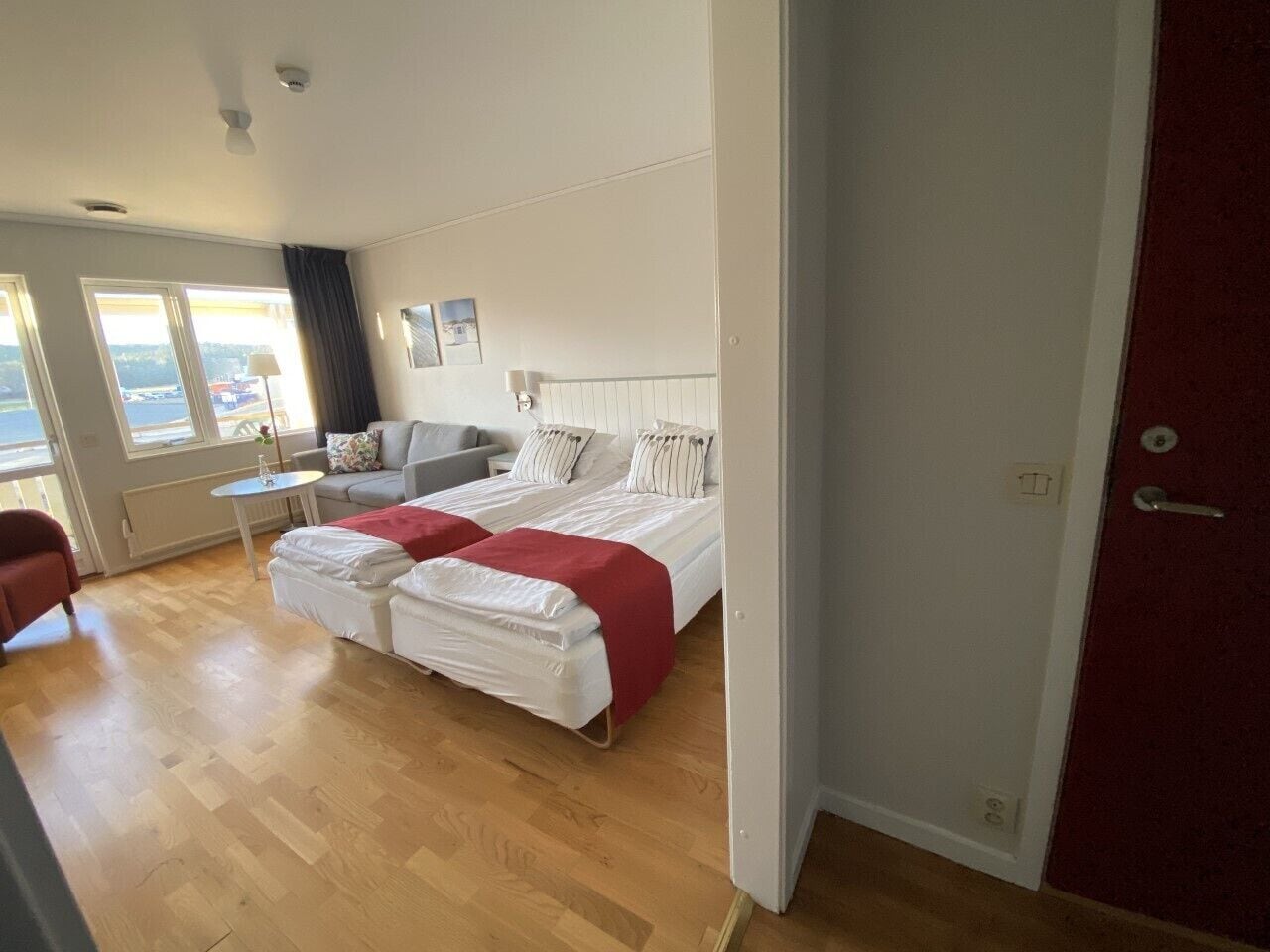 Une chambre d’hôtel moderne avec un grand lit, un canapé et une petite table. De grandes fenêtres offrent une vue sur l’extérieur.