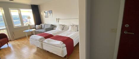 Ein modernes Hotelzimmer mit einem großen Bett, einer Couch und einem kleinen Tisch. Große Fenster bieten einen Blick ins Freie.