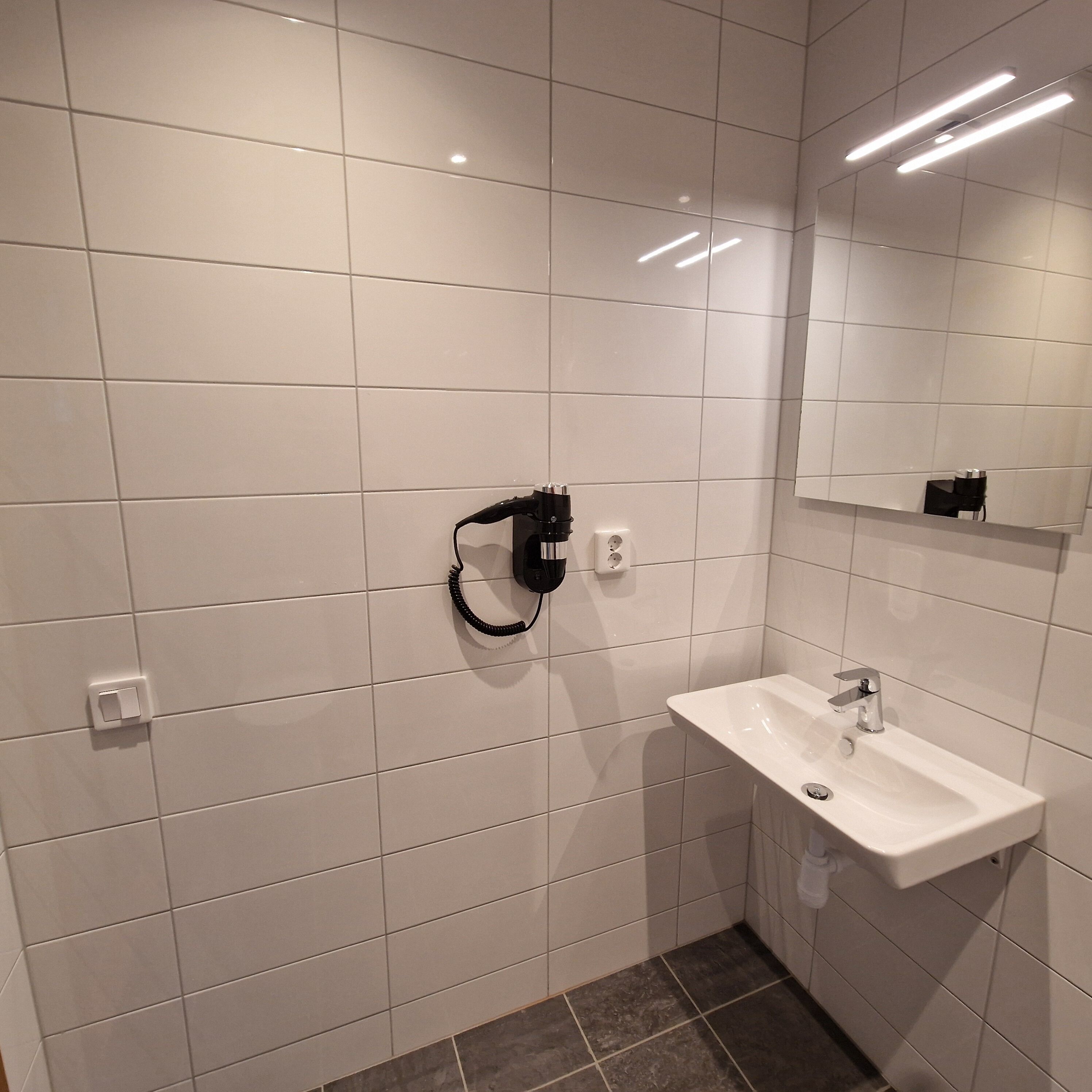 Un baño moderno con azulejos blancos, un lavabo, un espejo y un teléfono negro montado en la pared.