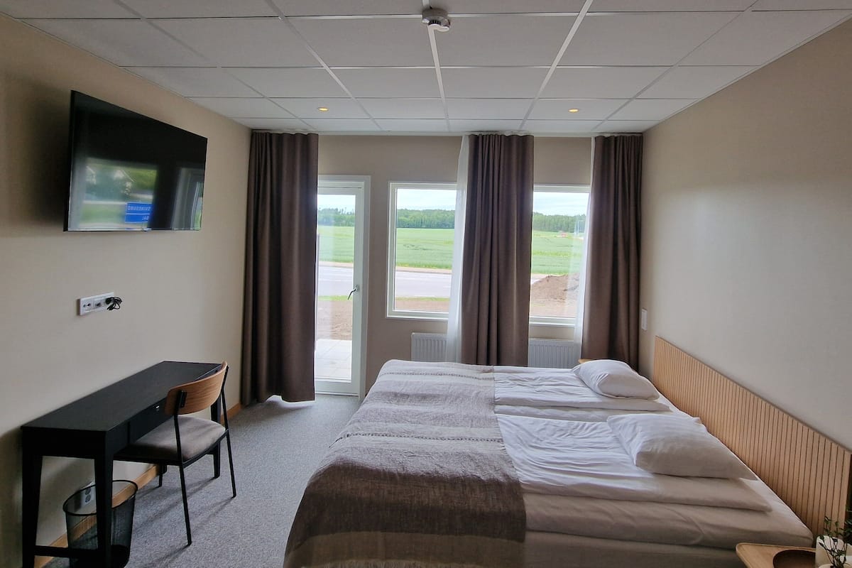 Habitación de hotel con cama, escritorio, silla, televisión y vistas al exterior.